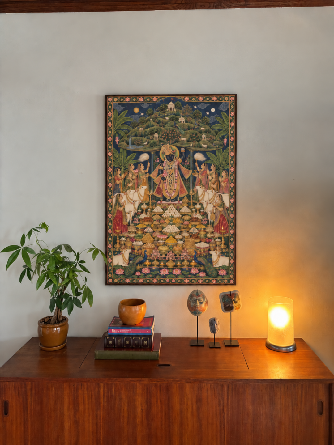 Shrinathji and the Mountain of Offerings art print shown framed above a wooden sideboard with a plant and lamp