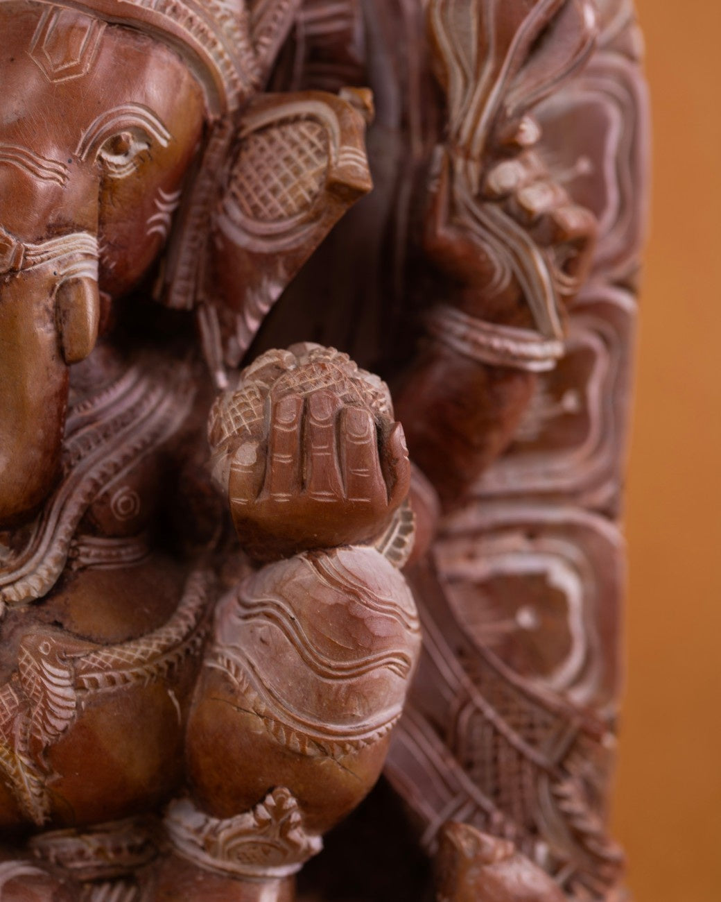 Detailed close‑up of red stone Ganesh sculpture showing him holding a modak