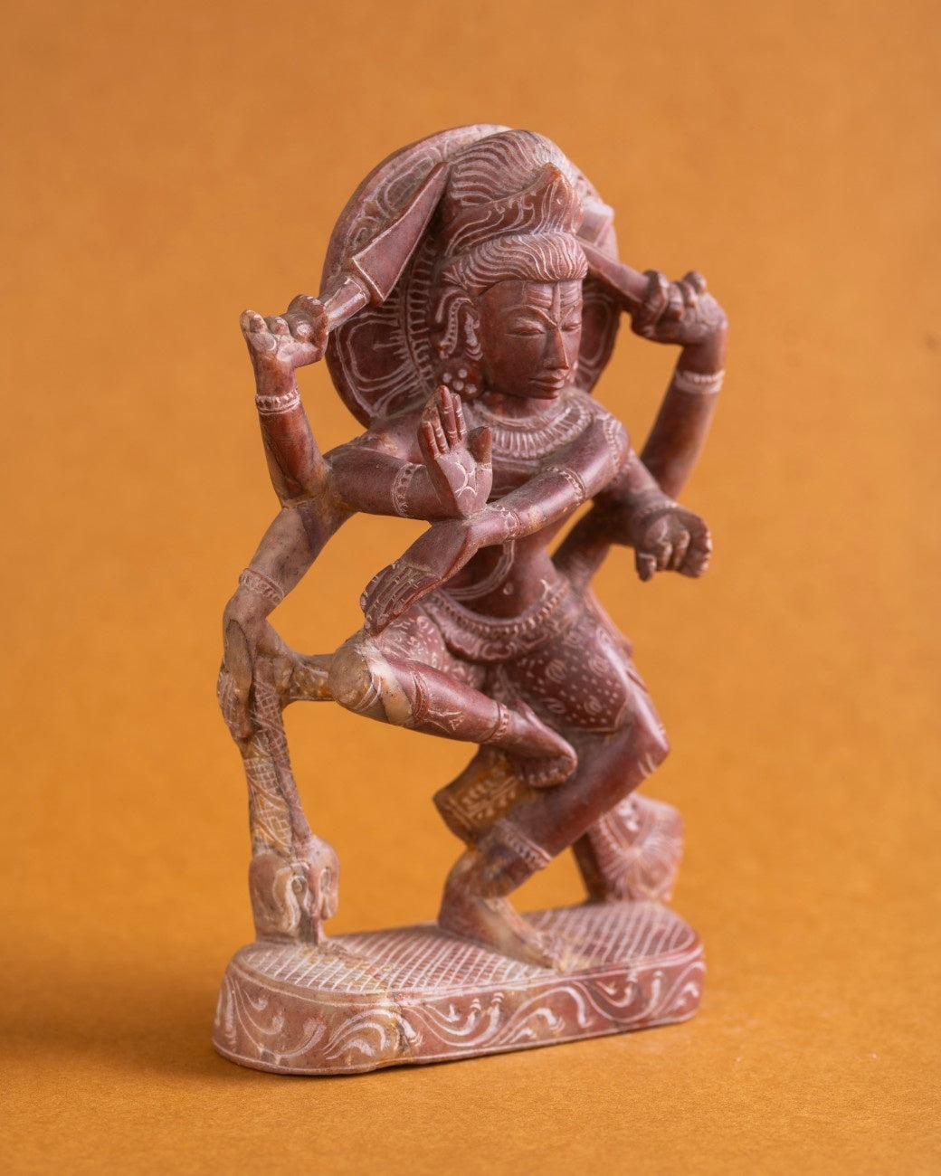 Side view red sandstone Shiva statue with raised foot and weapons.
