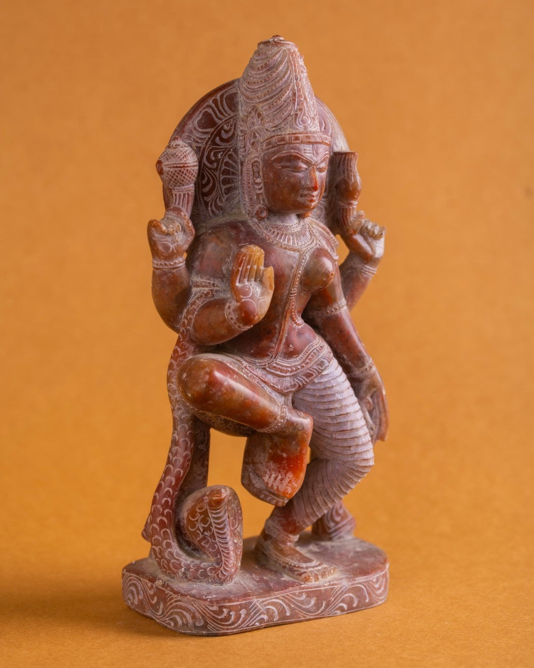 Hand-carved red stone Ardhanarishwar statue showing detailed hands, drapery, and ornamentation.