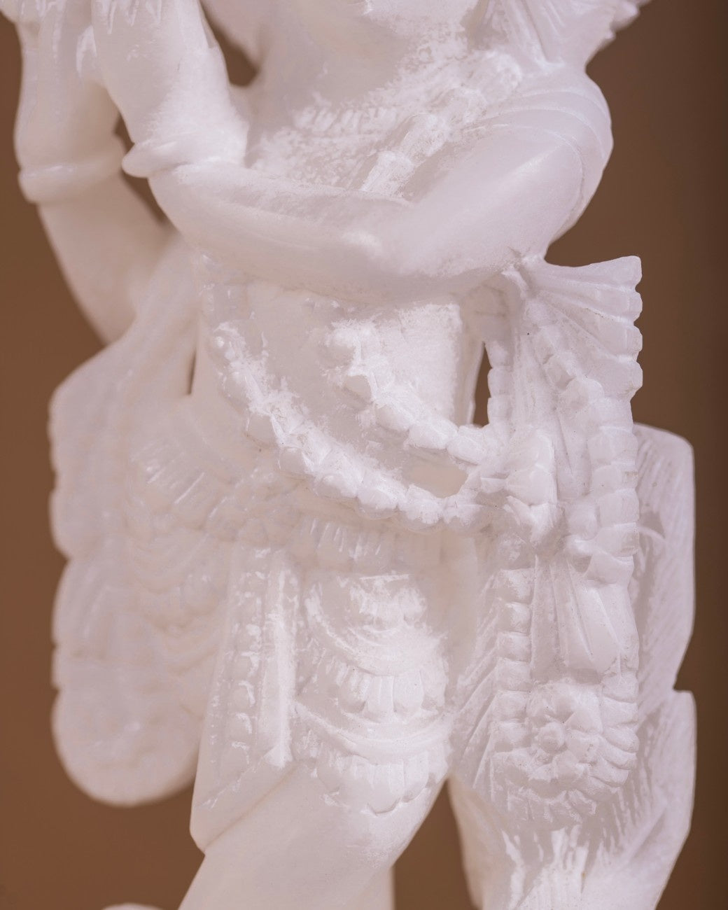 Krishna idol marble carving close-up displaying detailed attire and garland work.
