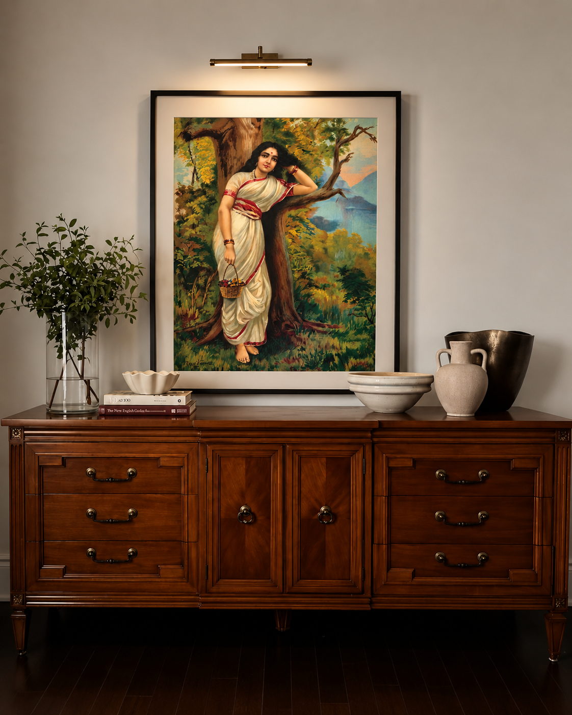 Framed print lit by a picture light above a dark wood sideboard with bowls and a plant