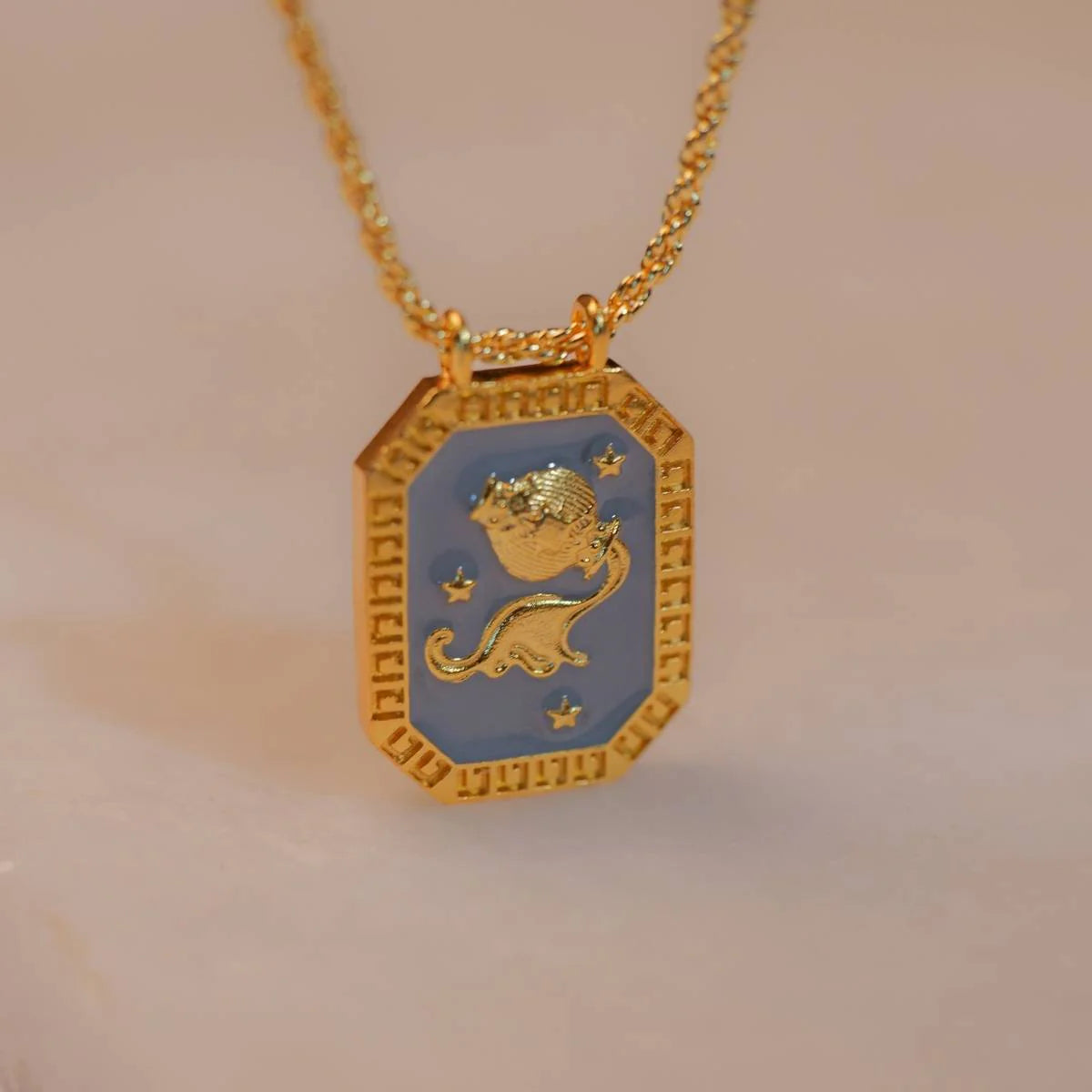 Reversible gold Aquarius pendant with amethyst back shown on soft fabric