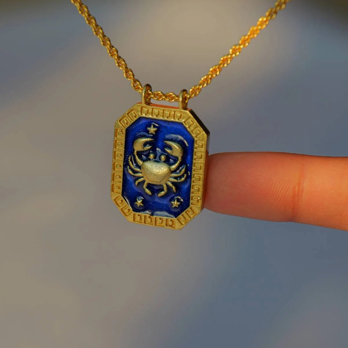 Close-up of gold Cancer zodiac necklace with blue enamel front and crab motif