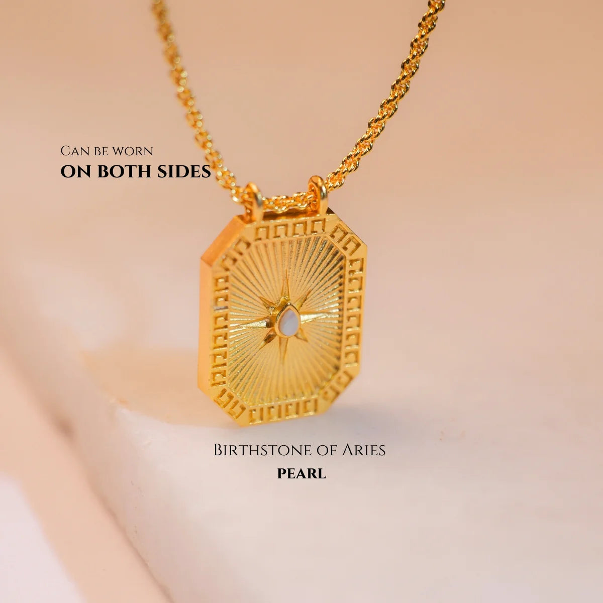 Reversible gold Gemini zodiac pendant with pearl back shown on soft fabric