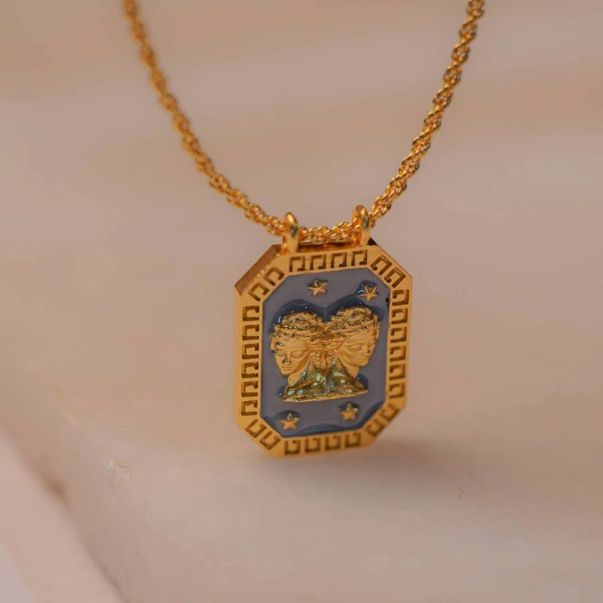 Close-up of gold Gemini zodiac tablet necklace with enamel front and twin motif