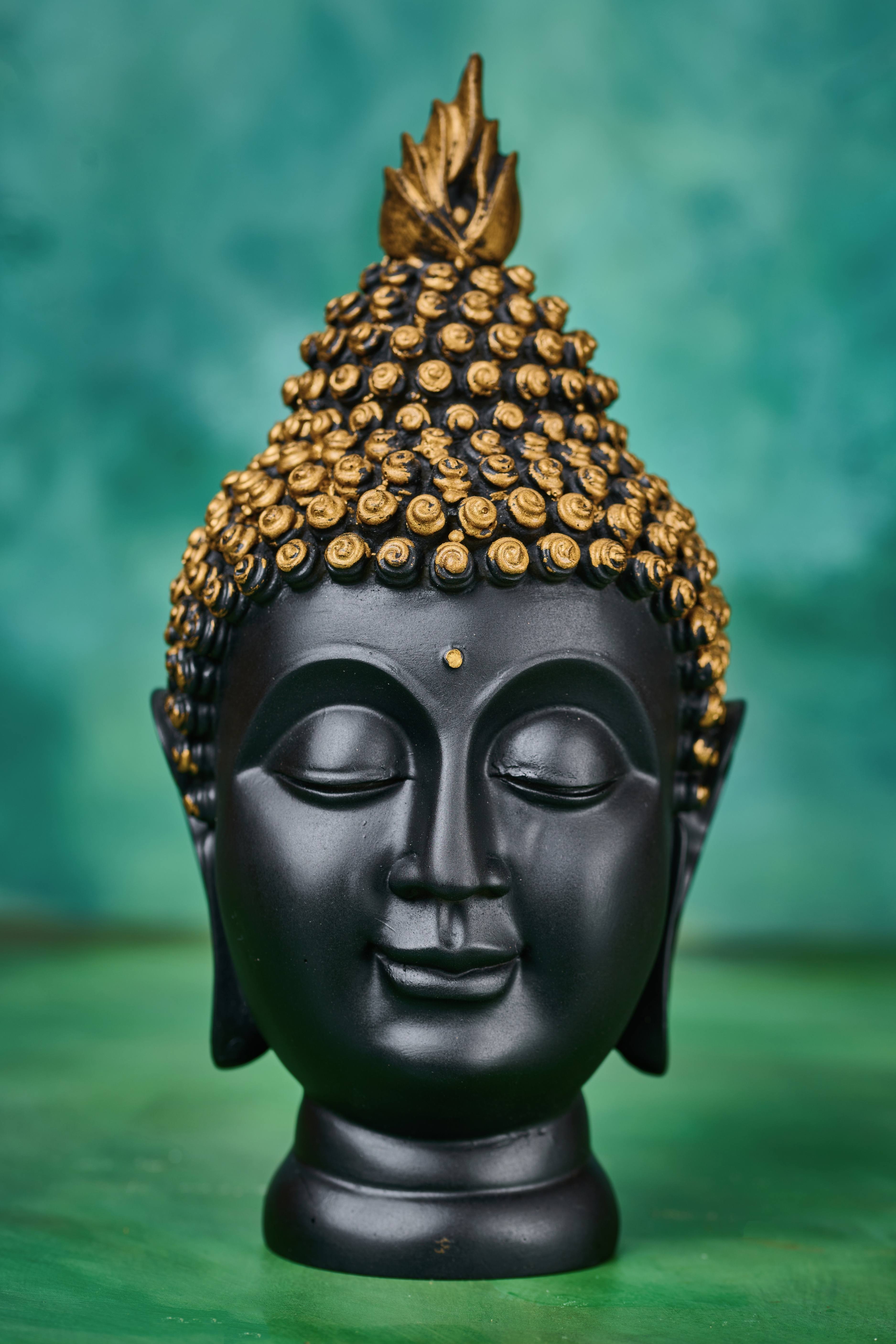 Detailed close-up of Buddha face in black resin with gold crown – serene meditation decor accent