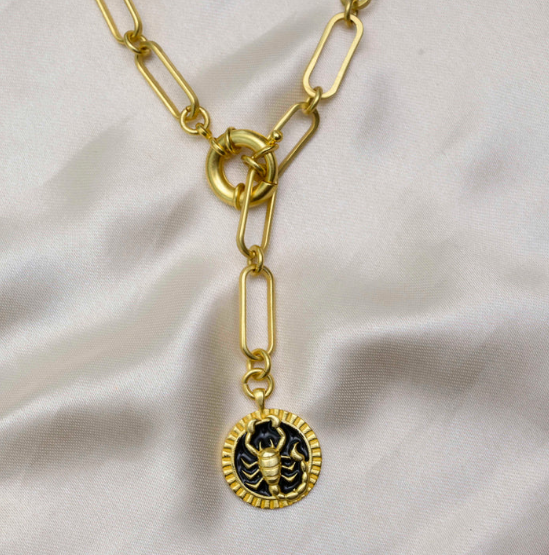 Gold Scorpio medallion necklace with paperclip chain displayed on soft fabric