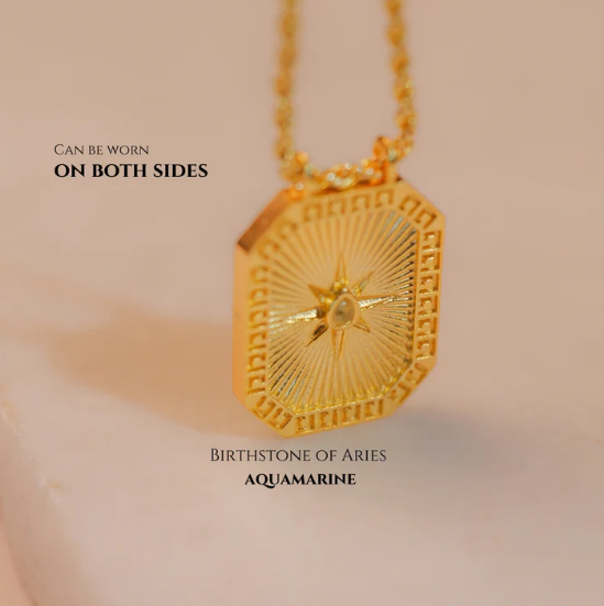 Reversible gold Pisces pendant with aquamarine back shown on soft fabric