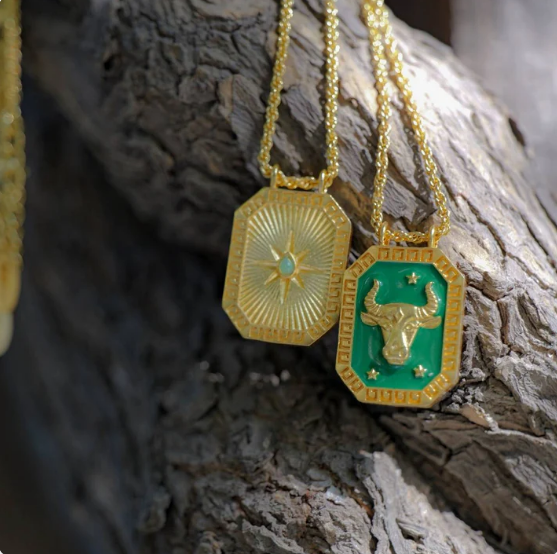 Outdoor close-up of gold Taurus zodiac necklace with green enamel front and bull motif