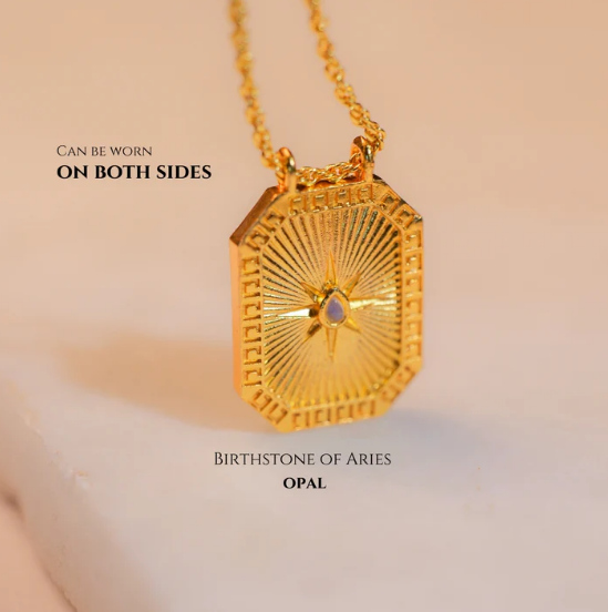 Reversible gold Libra pendant featuring opal back shown on soft fabric