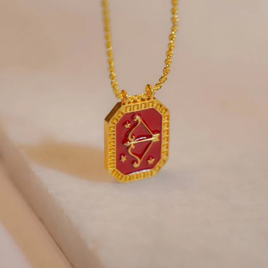 Red enamel Sagittarius zodiac tablet pendant shown on soft fabric