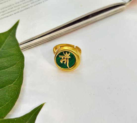Gold Ma ring with malachite stone placed beside green leaf