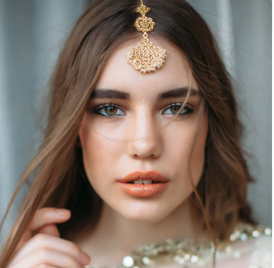 Model wearing gold floral maang tikka styled with bridal makeup and embellished outfit