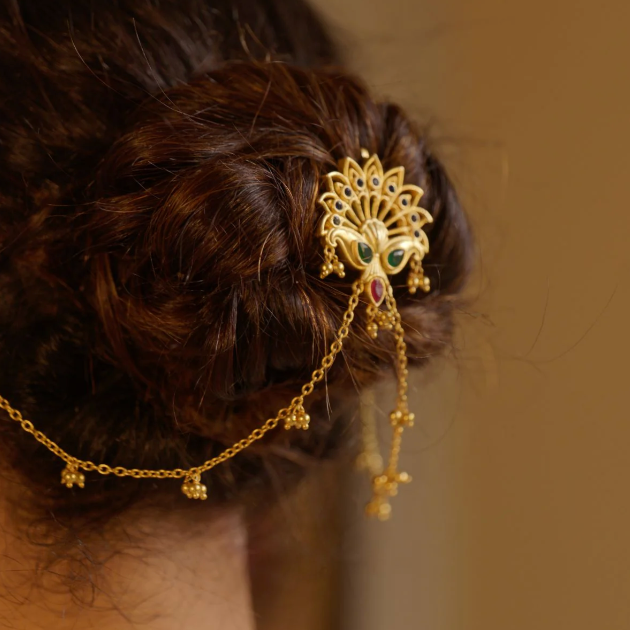 Back view of bridal bun adorned with gold peacock juda pin and cascading charm chains