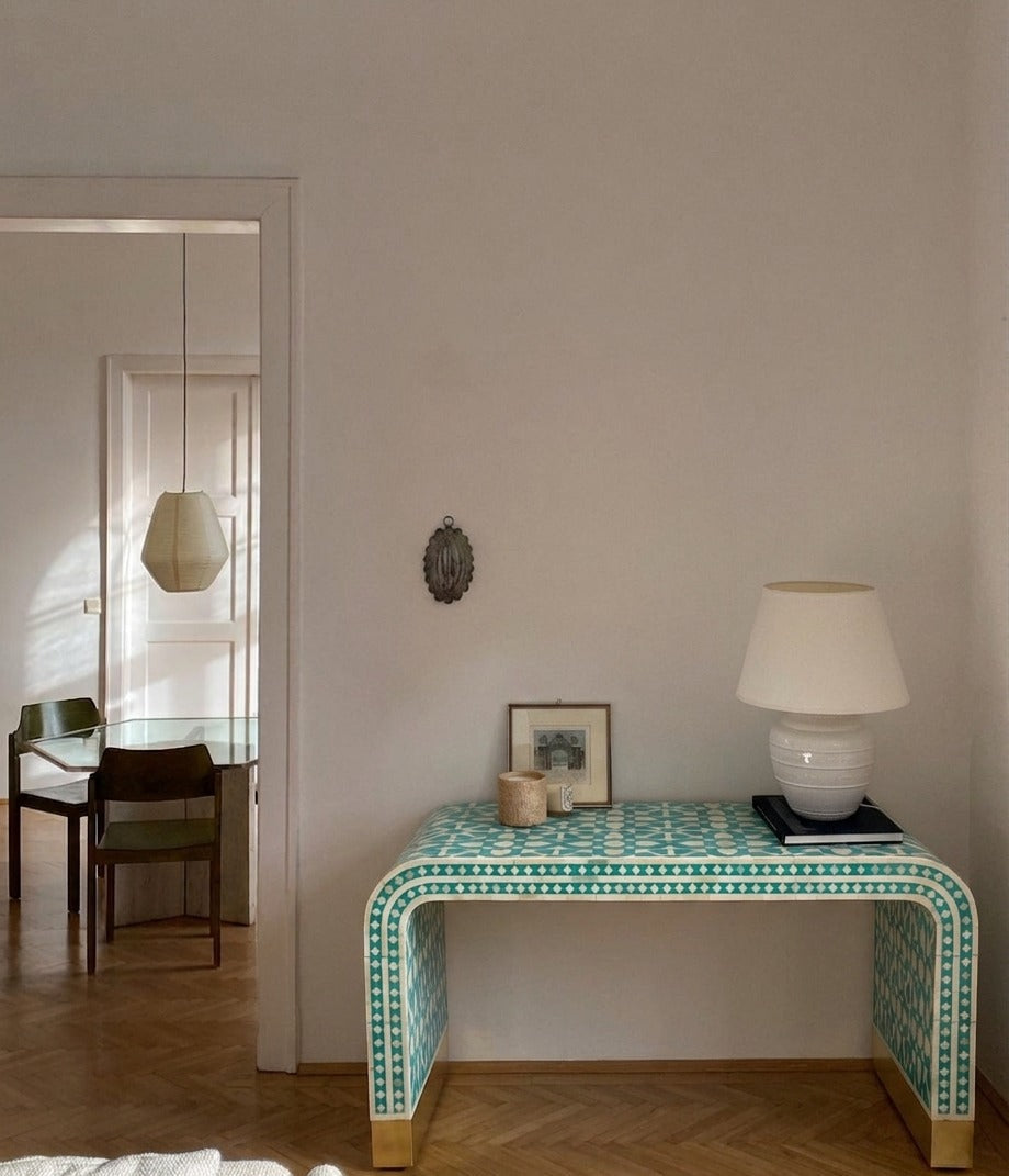 Decorative table with green pattern in a room with a lamp and framed picture.