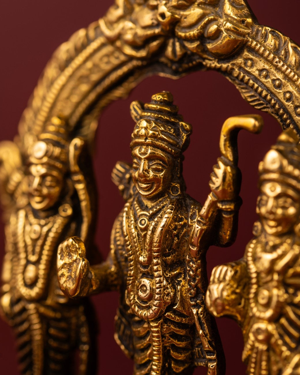 Close-up of brass Ram Darbar figurine showing detailed carving of Rama, Sita, and Lakshmana in temple-style artwork.
