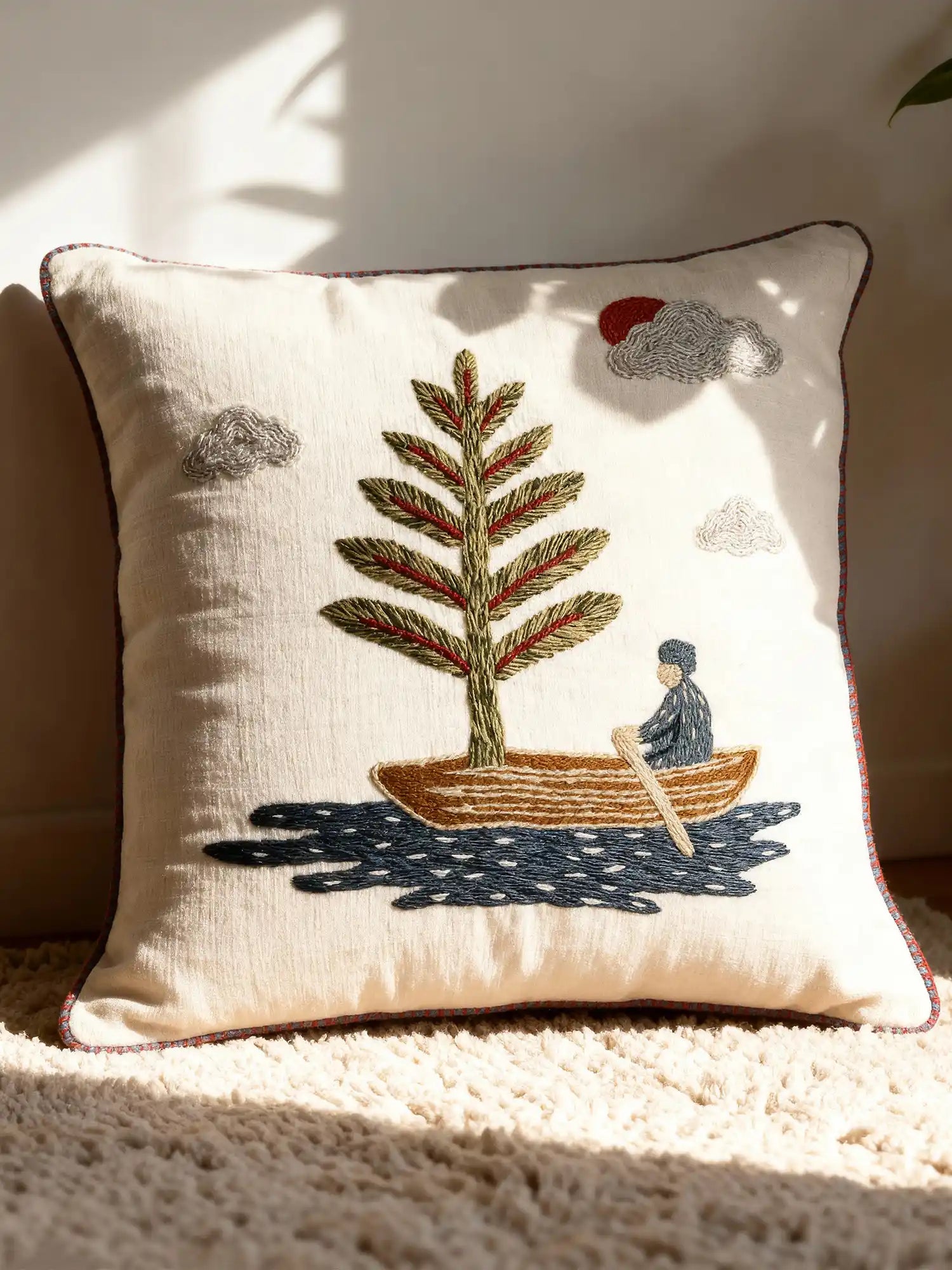 A luxury Celestial Village cushion cover featuring hand-embroidered landscape motifs and red piping on a tan velvet sofa.