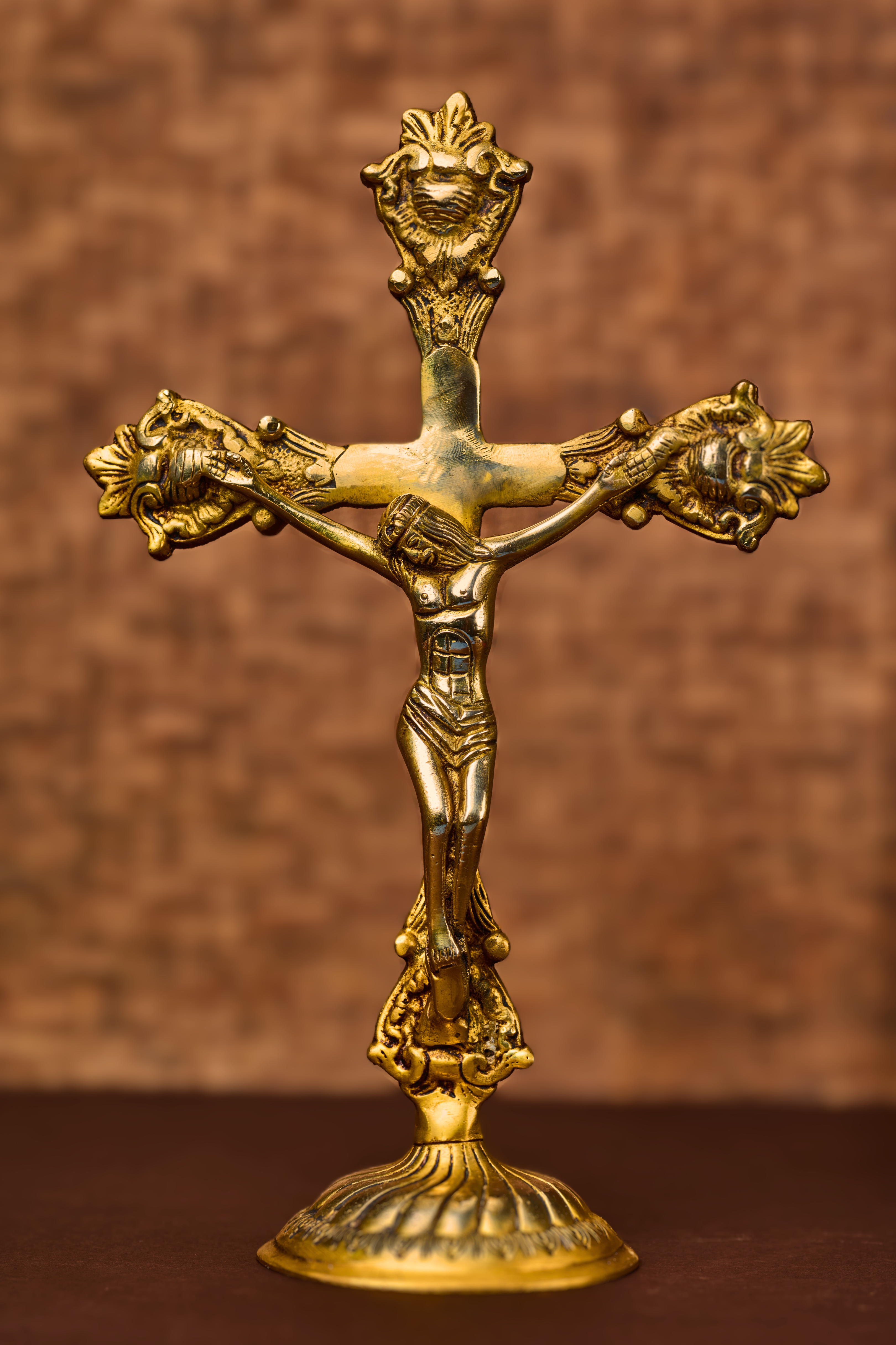 Solid brass sculpture of Christ on a cross with etched details and ornate base, displaying golden color.