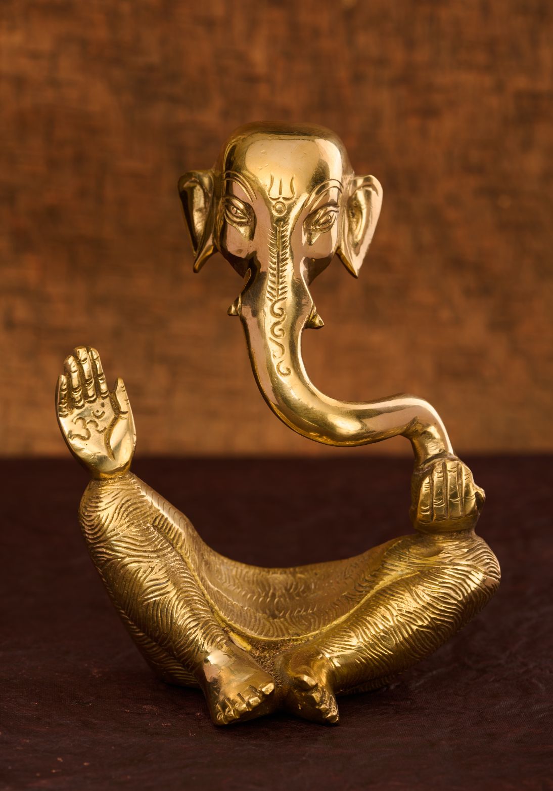 A brass sculpture of Lord Ganesha, the Hindu deity with an elephant face, sitting with his hands raised in blessing.