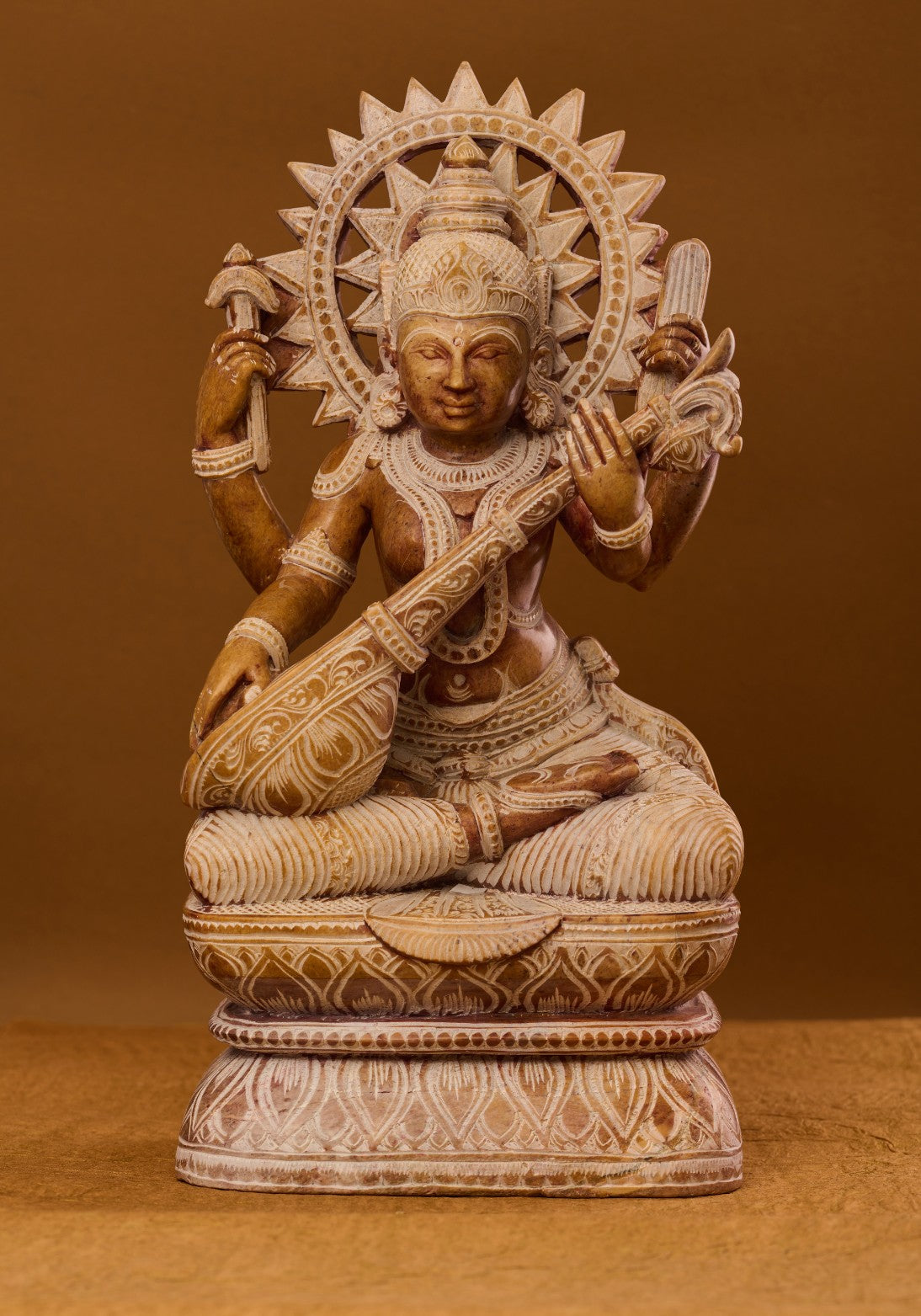 A sculpture of the Hindu goddess Saraswati, seated and holding a musical instrument, carved from red stone with intricate details.