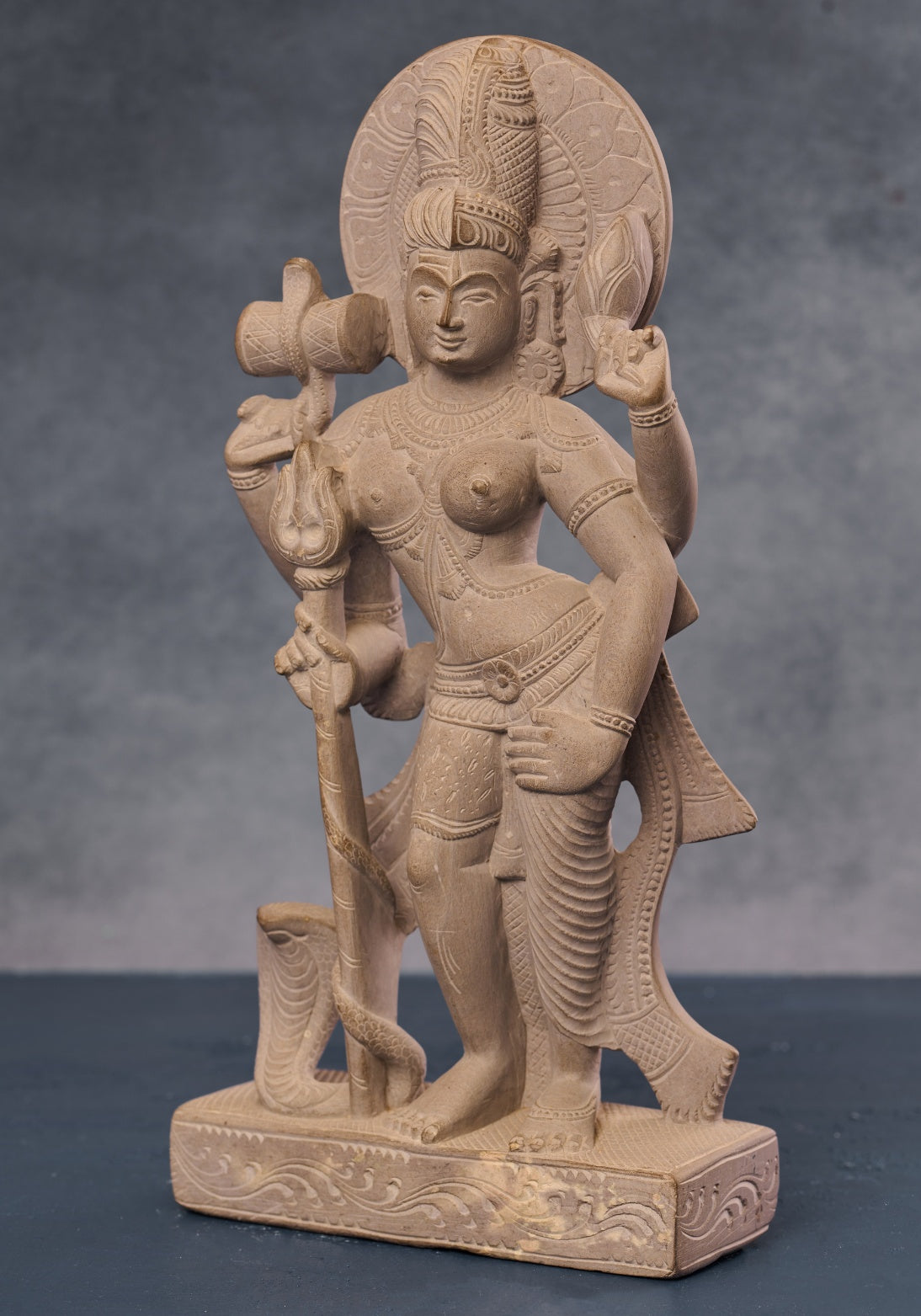 Angled view of stone Ardhanarishvara statue with detailed carving, symbolic half-male half-female Hindu idol.