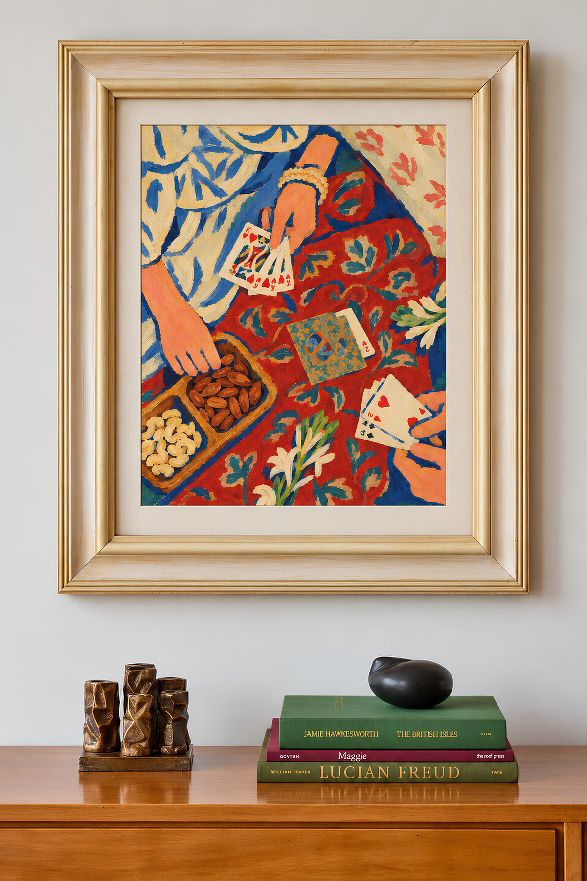 Framed card-game painting on a wall above a wooden sideboard with books and small wooden sculptures