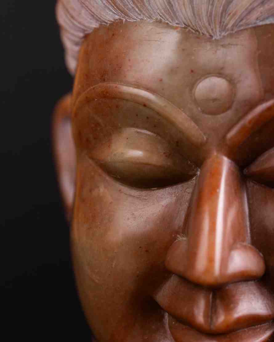 Close‑up of red stone Buddha head showing detailed serene facial features buy now