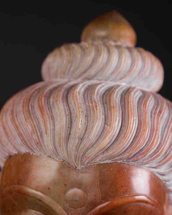 Close‑up of red stone Buddha head showing detailed ushnisha topknot and carved facial features