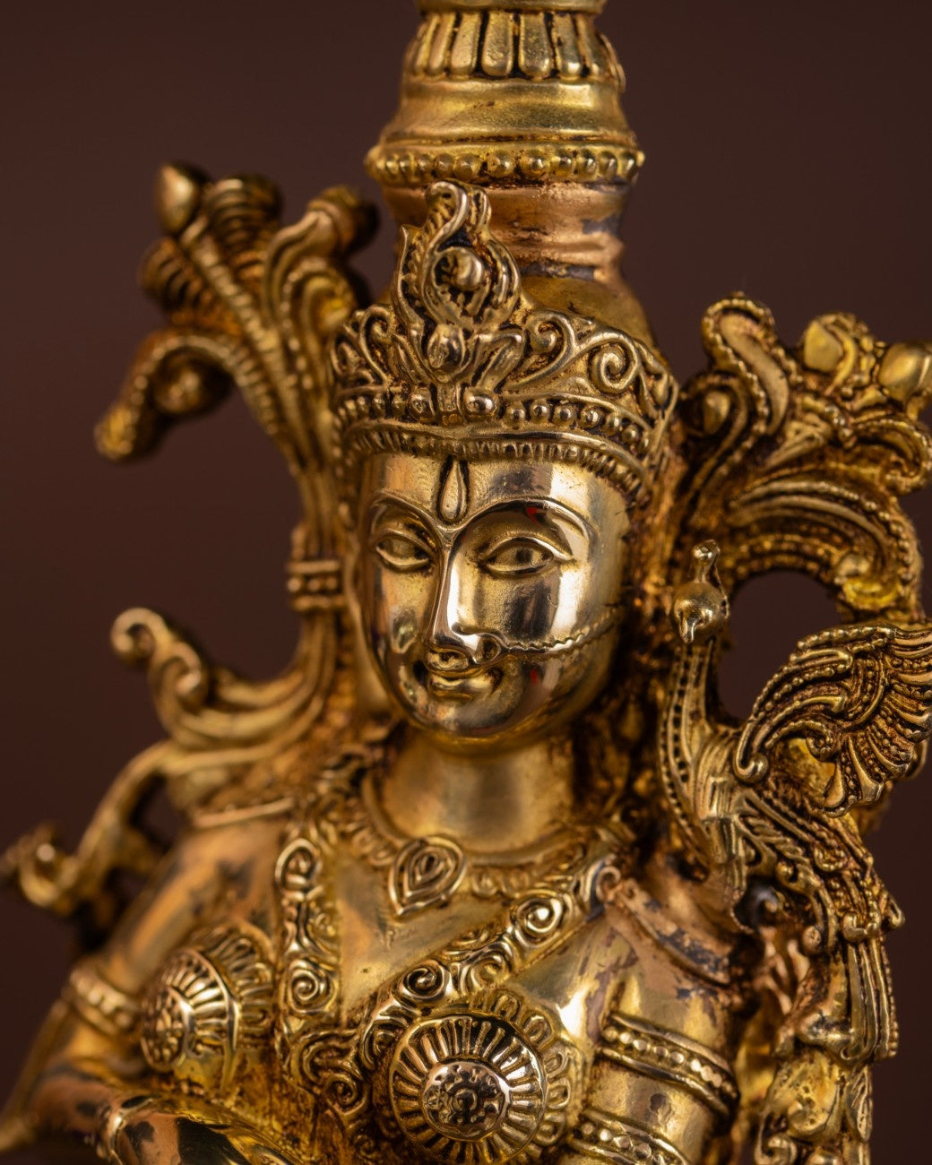 Close-up of brass Radha sculpture showing facial features, crown detailing, and traditional Indian deity jewellery.