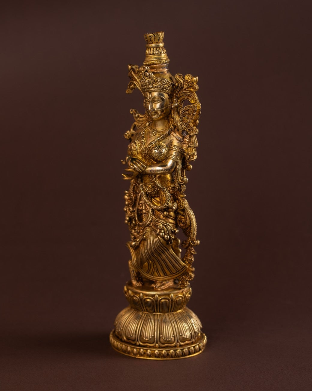 Angled view of handcrafted brass Radha idol with intricate sari patterns and temple-style metalwork.