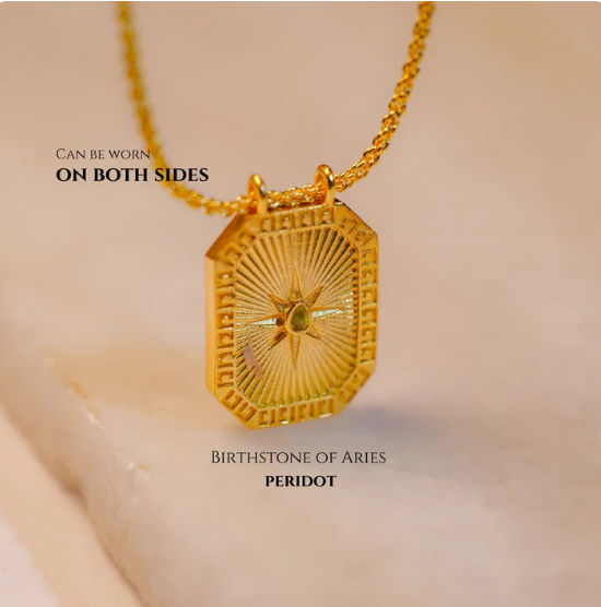 Reversible gold Leo zodiac pendant with peridot gemstone back on soft fabric