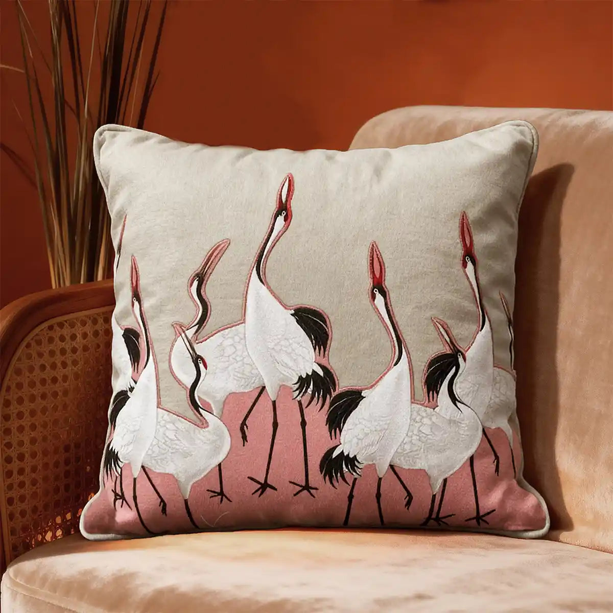 Sedge Pink cushion cover with embroidered cranes on a pink patch, styled on a sofa in moody lighting.