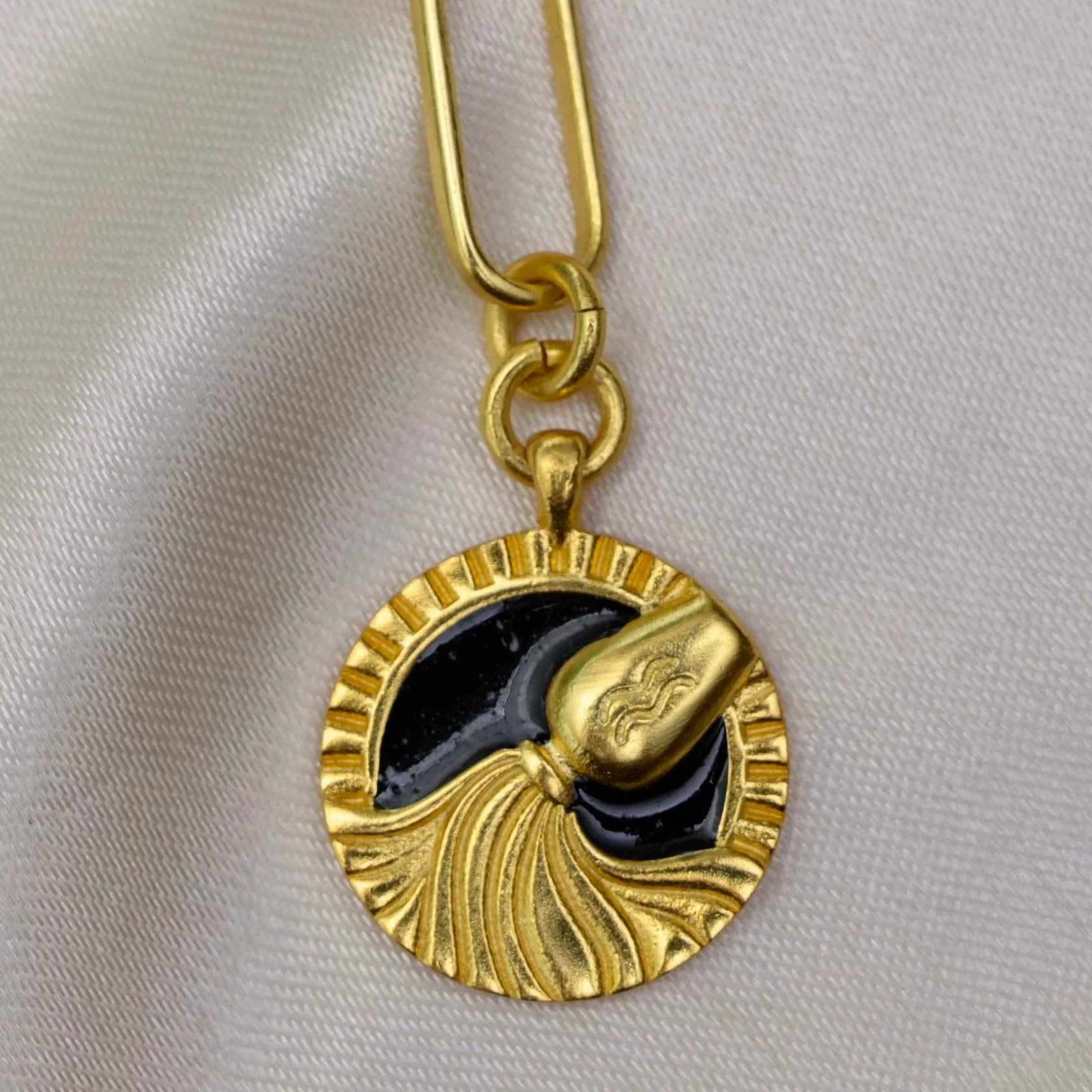 Close-up of gold Aquarius pendant with black enamel water-bearer design