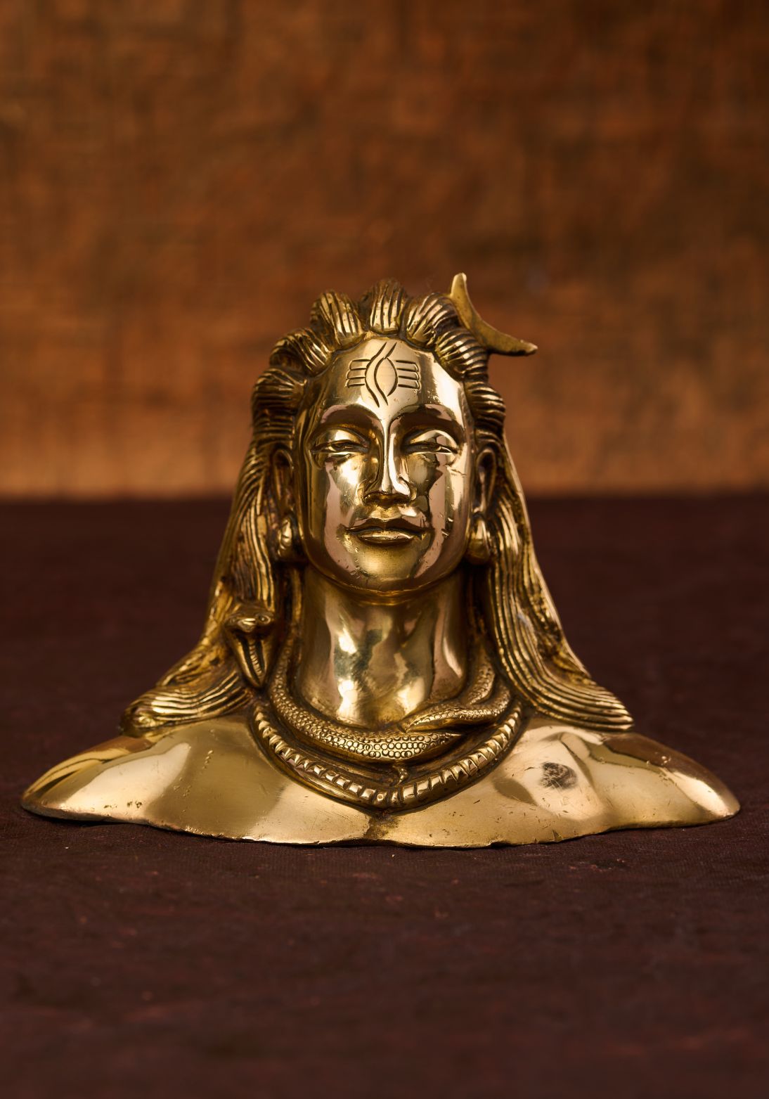 A brass sculpture of Lord Shiva with a meditative expression, featuring a snake coiled around his neck and his third eye.