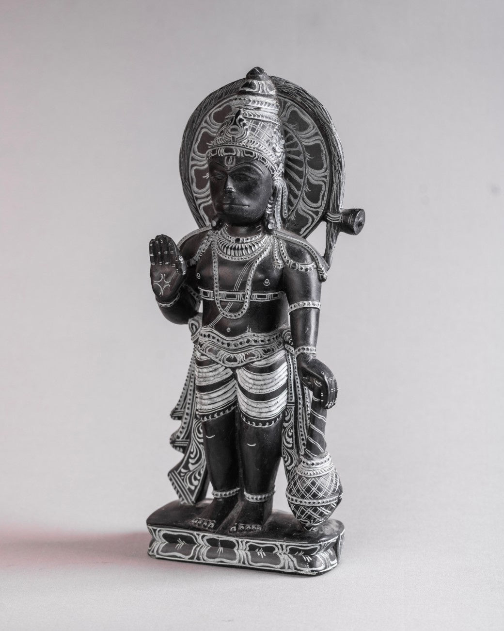 Black stone Hanuman statue in standing pose holding mace and raising hand in protection gesture.
