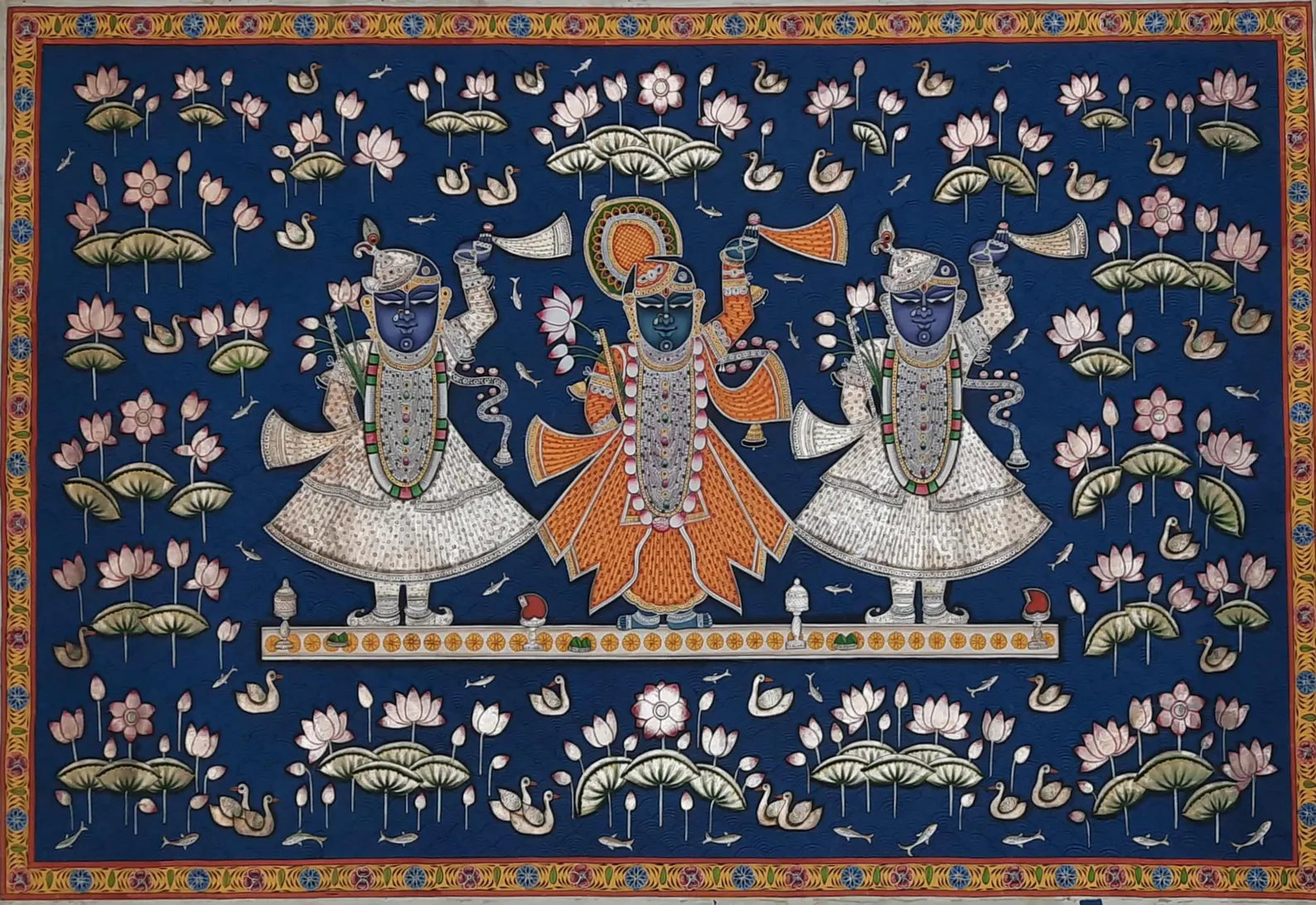 Hand-painted Pichwai artwork depicting Lord Shrinathji adorned with jewelry and lotuses against a deep blue background, surrounded by sacred motifs