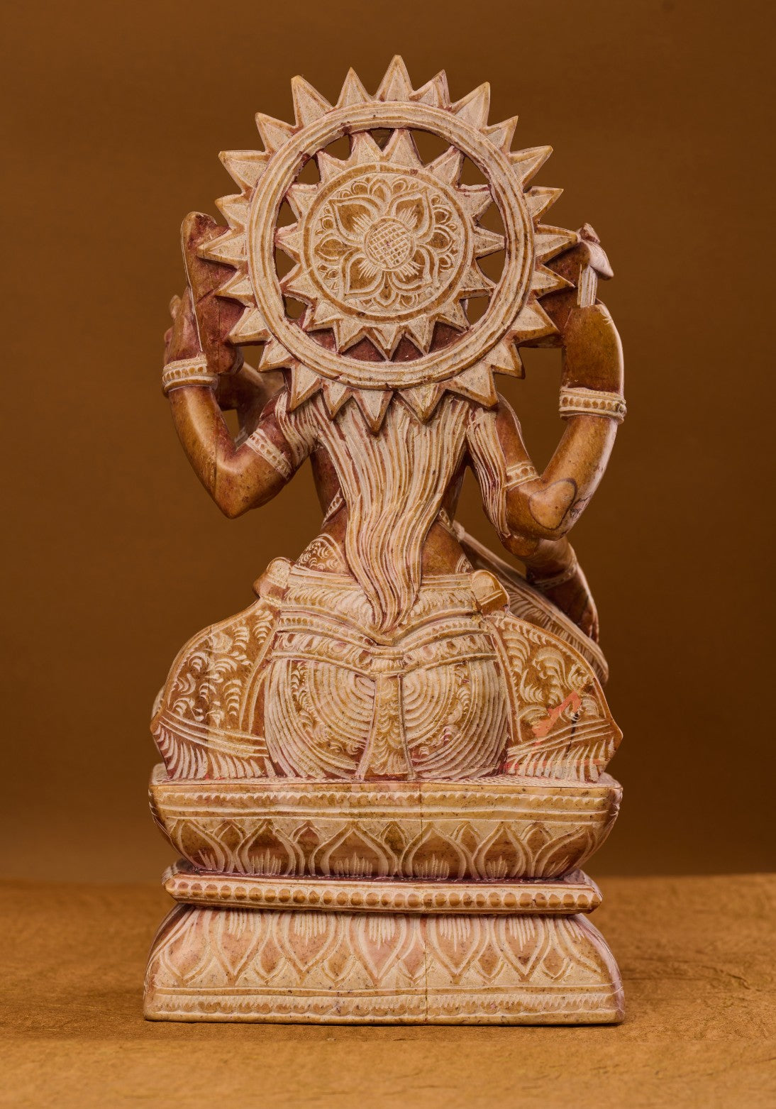 Back view of red stone Saraswati statue highlighting single‑block craftsmanship and texture