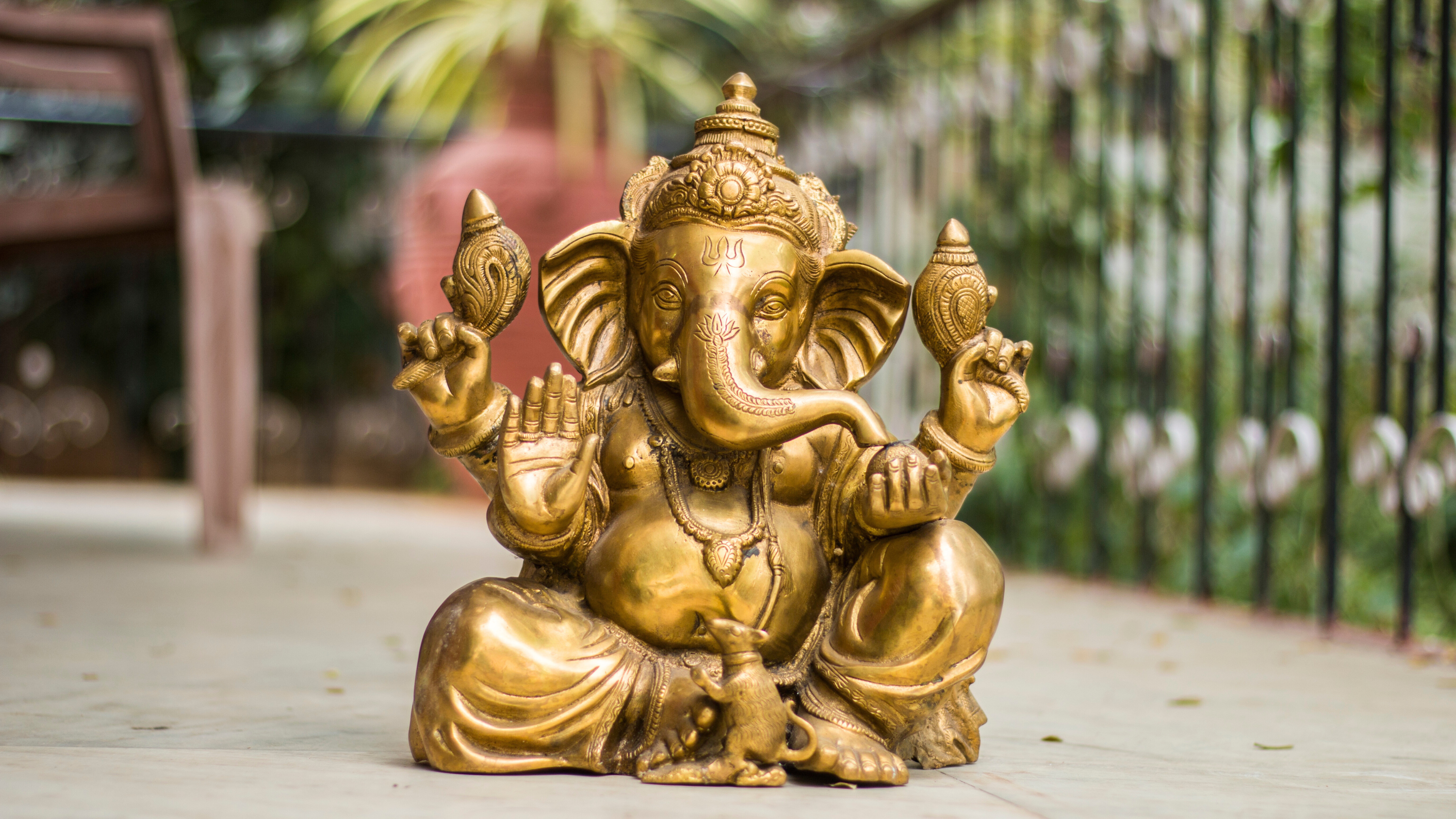 Handcrafted brass Ganesh idol placed in outdoor home setting, traditional Hindu remover of obstacles sculpture.