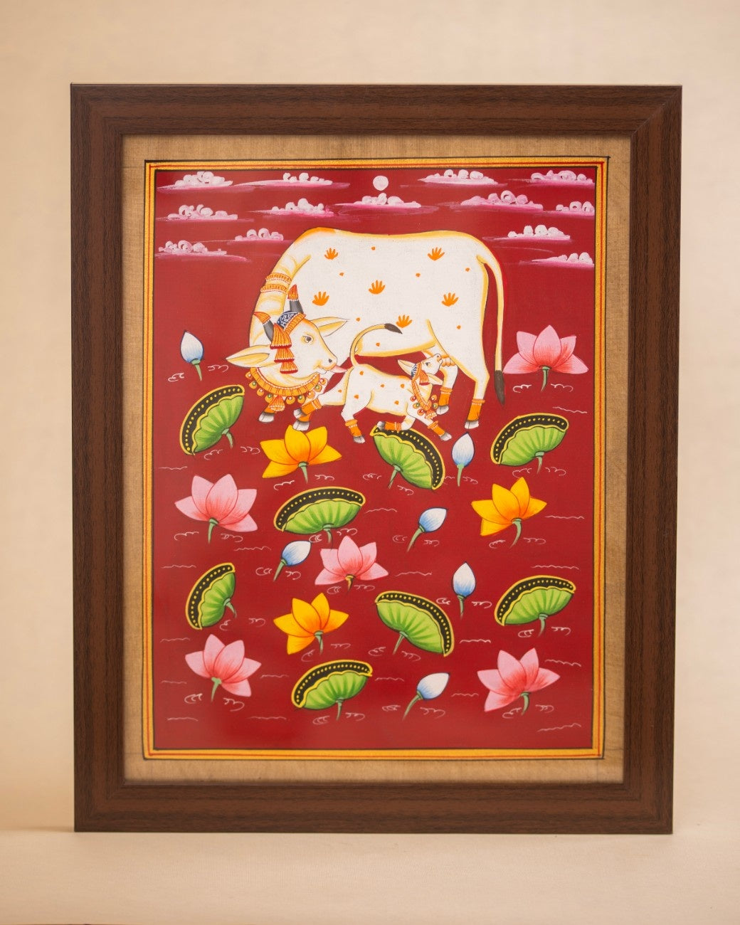 Framed traditional Indian cow painting with floral motifs on a red background